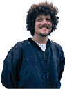 A person with curly hair is smiling and wearing a dark blue zip-up jacket over a white shirt against a white background. Description generated by AI